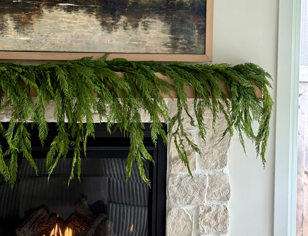 Framed landscape painting above a stone fireplace with realistic greenery.