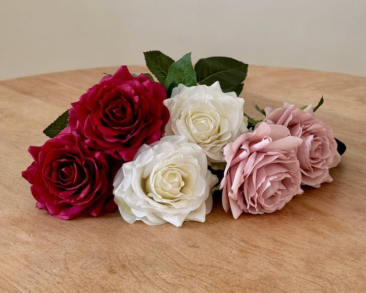 six real touch roses in red, white, and pink on a wooden surface with a plain background