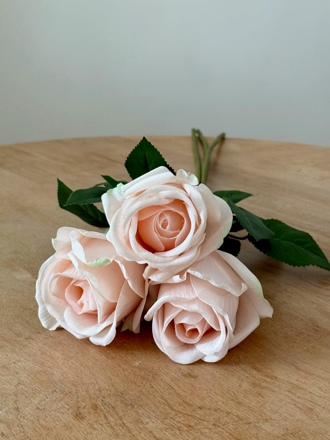 Bouquet of pink luxury artificial roses on a wooden surface with a light background